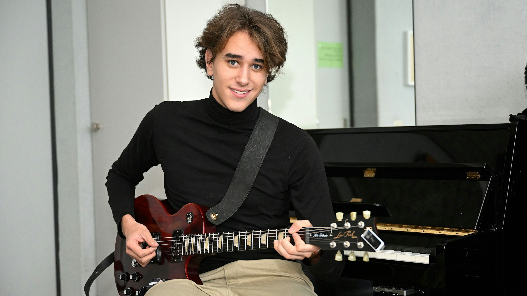 Yves Richter, 19 Jahre alt, sitzt mit einer roten Gitarre in der Hand vor einem Klavier.