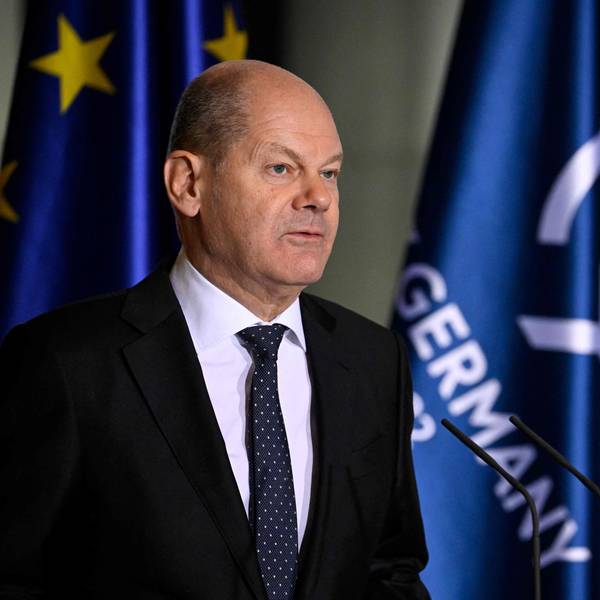 Olaf Scholz im Vordergrund steht vor Mikros und redet. Im Hintergrund sind die europäische Flagge und die der G7 zu sehen.