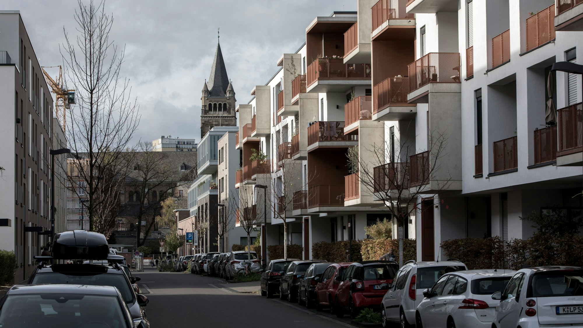 Das Bild zeigt eine Straße mit Parkplätzen und Autos und einer Kirche im Hintergrund.