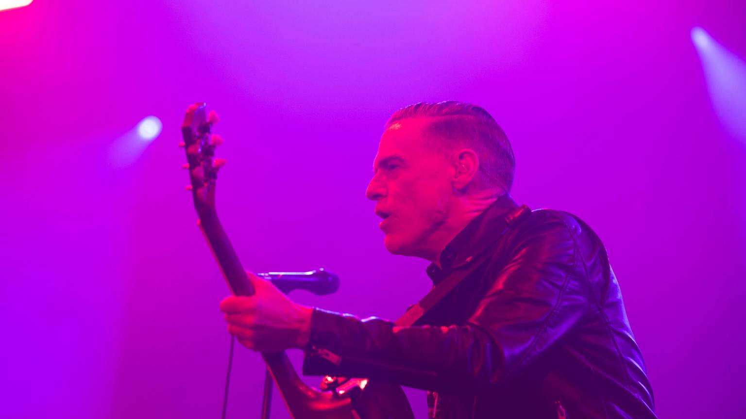 Bryan Adams steht mit Gitarre auf der Bühne und singt.