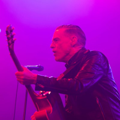 Bryan Adams steht mit Gitarre auf der Bühne und singt.