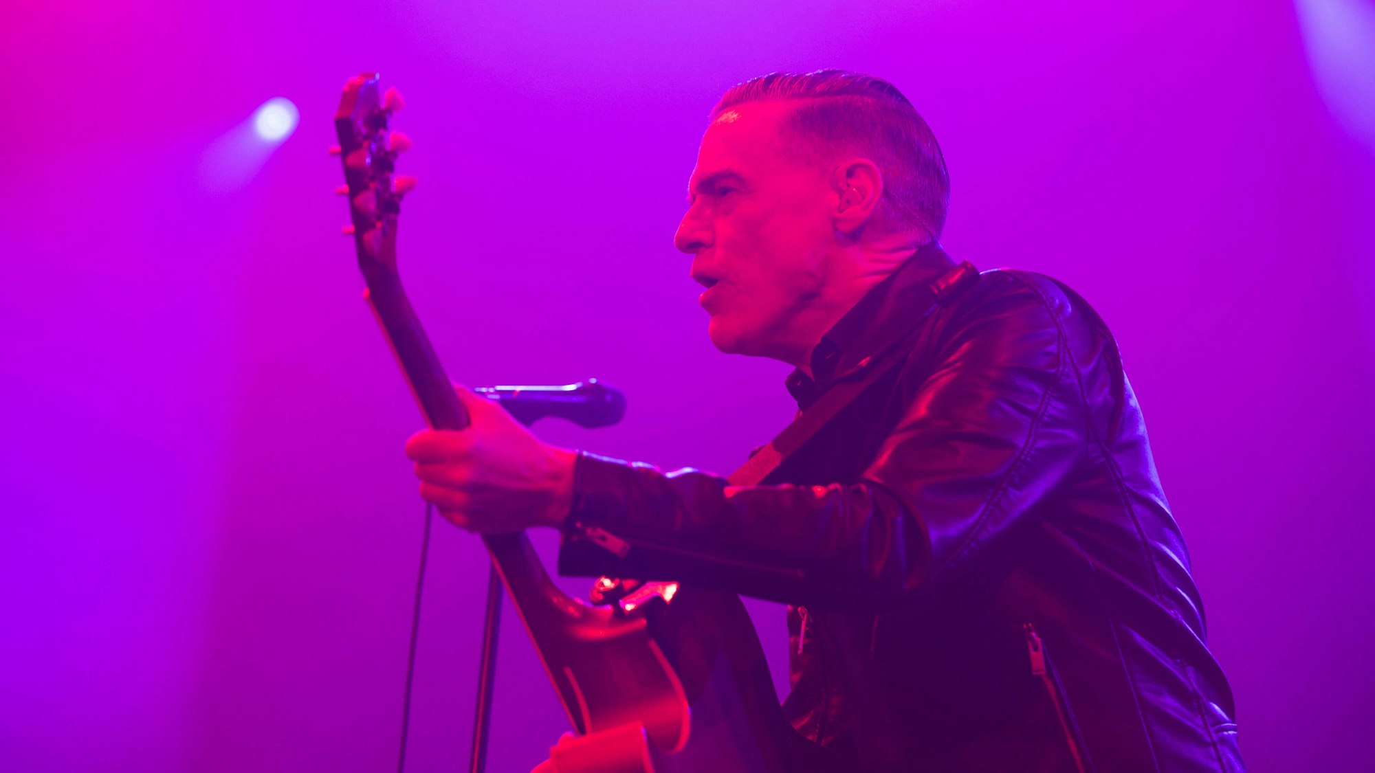 Bryan Adams steht mit Gitarre auf der Bühne und singt.