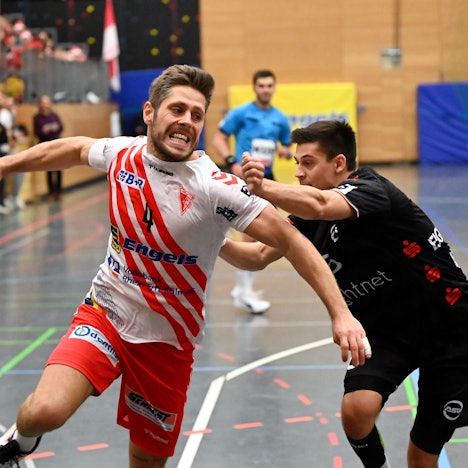 Ein Handballspieler wird von seinem Gegner beim Torwurf bedrängt.