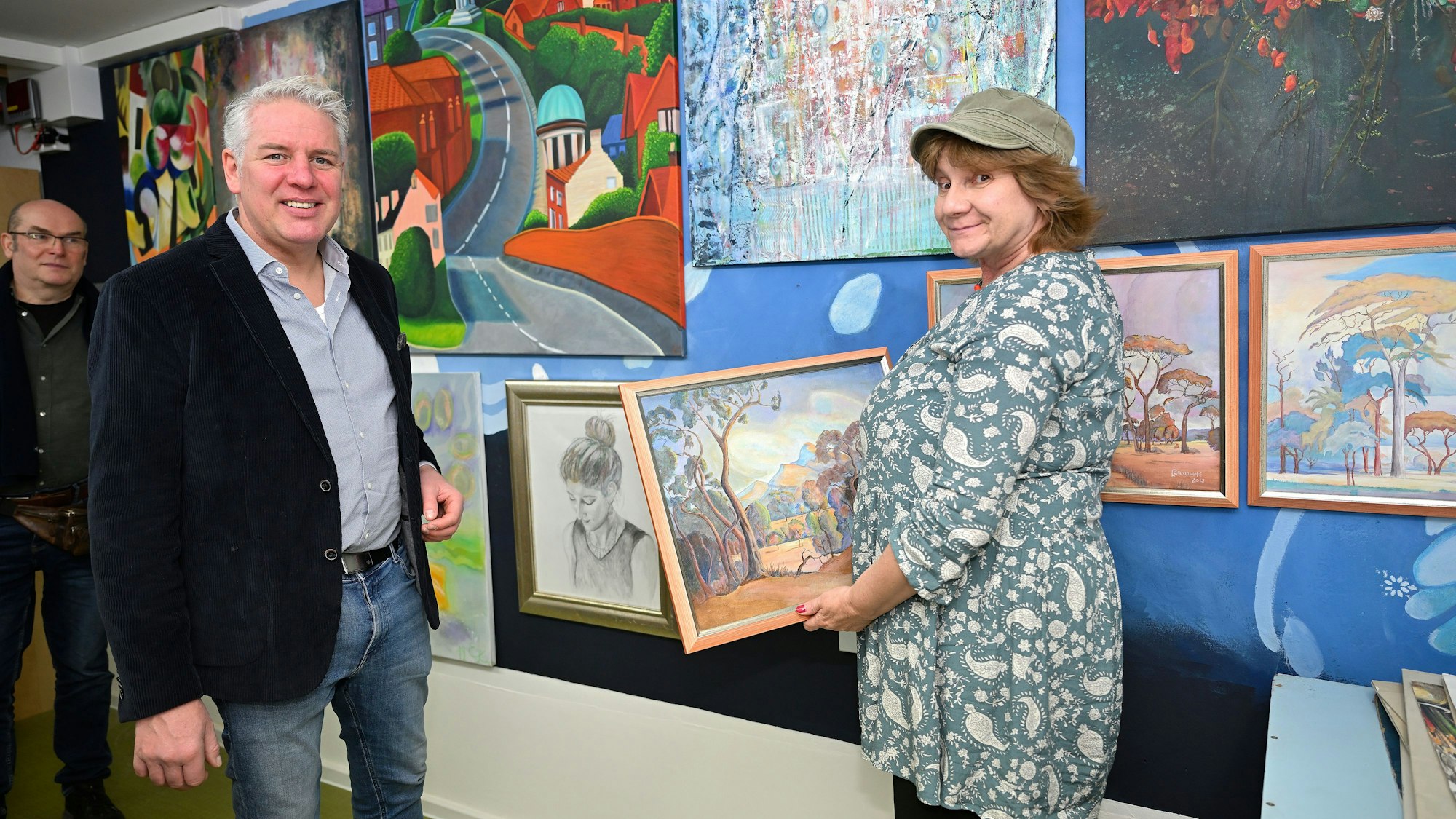Odenthals Bürgermeister Robert Lennertz und Berret Smith stehen vor einer Wand voller Gemälde.