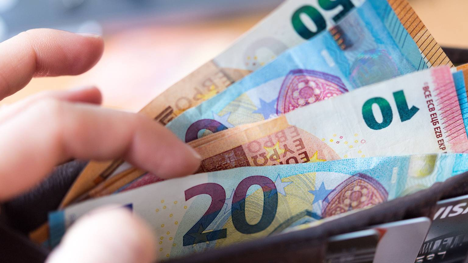 Eine Frau hält eine Geldbörse mit Banknoten in der Hand und zieht einen 20-Euro-Schein heraus.