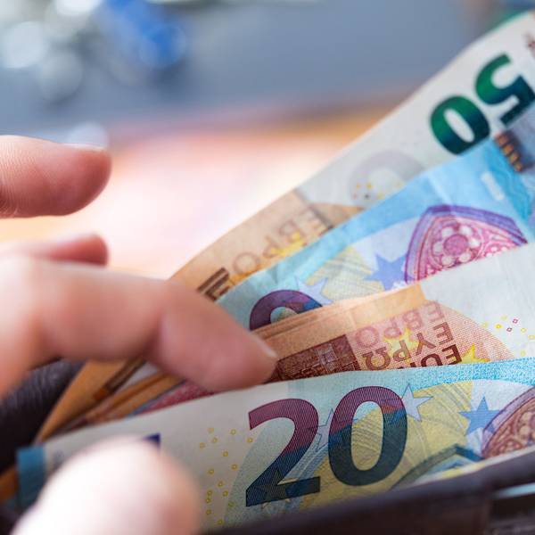 Eine Frau hält eine Geldbörse mit Banknoten in der Hand und zieht einen 20-Euro-Schein heraus.