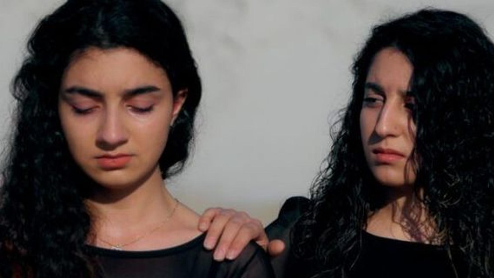 Zwei junge geflüchtete Frauen mit traurigem Blick geben sich Hoffnung. Die eine fasst der anderen schützend auf die Schulter.