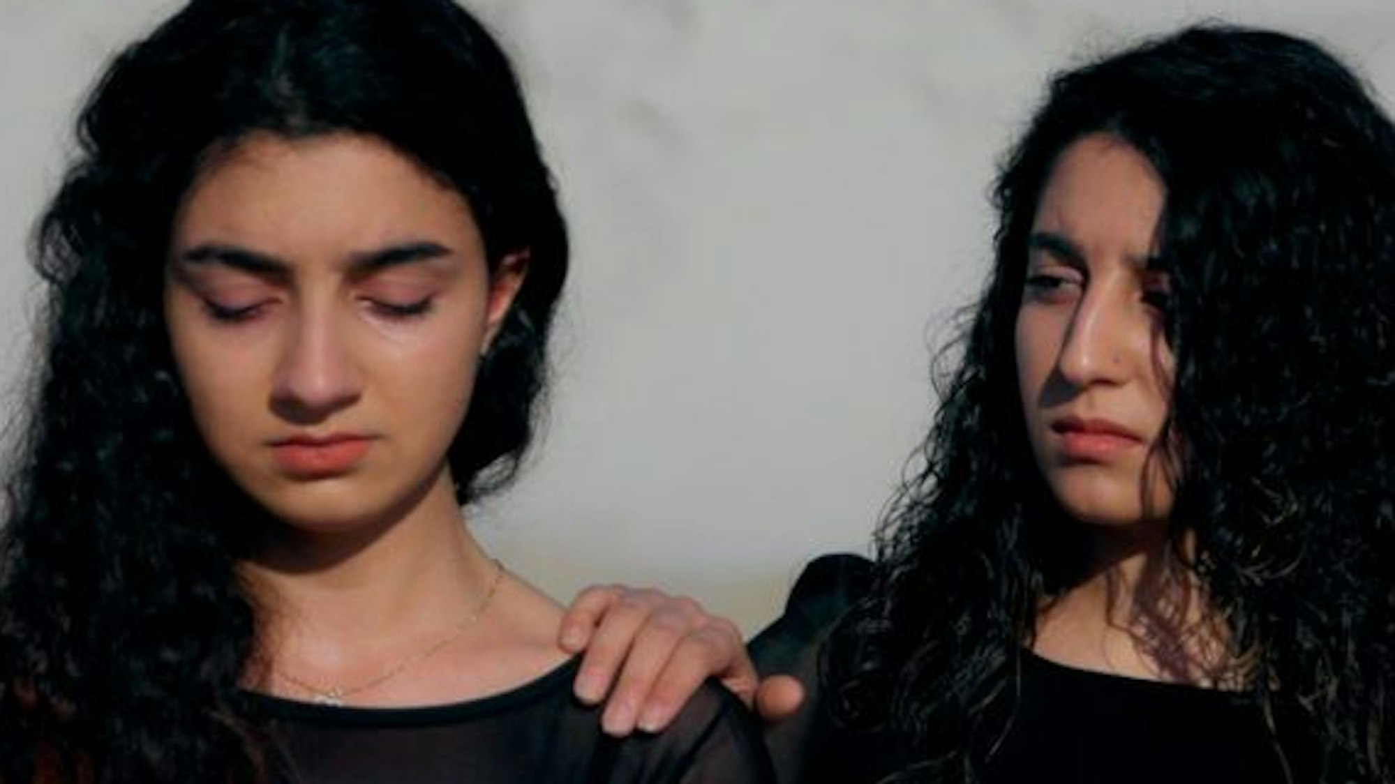 Zwei junge geflüchtete Frauen mit traurigem Blick geben sich Hoffnung. Die eine fasst der anderen schützend auf die Schulter.