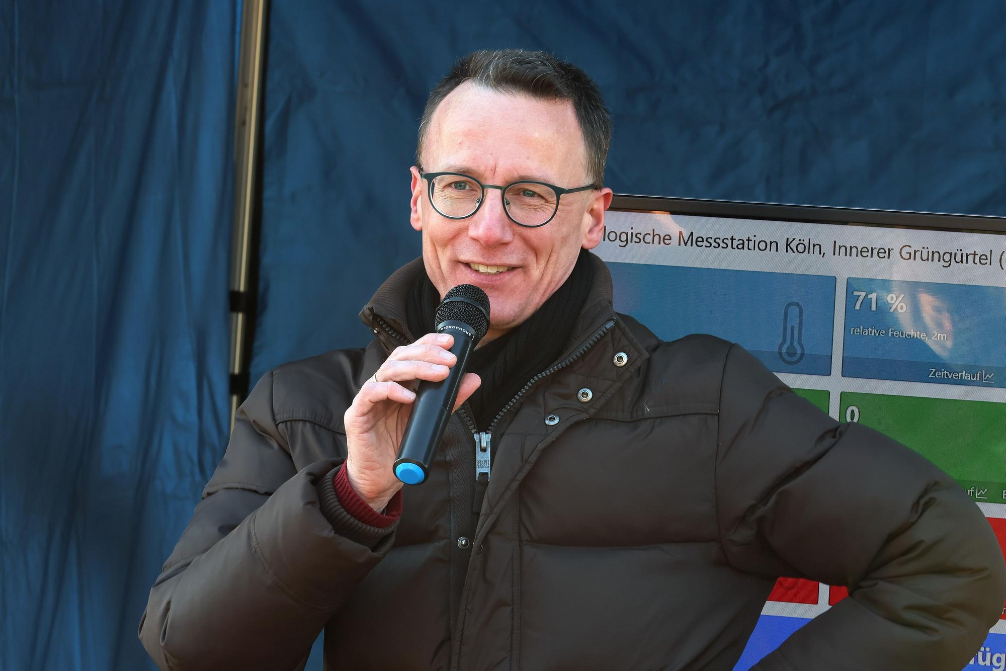 Der Professor in Winterjacke und mit runder Brille an einem Mikrofon.