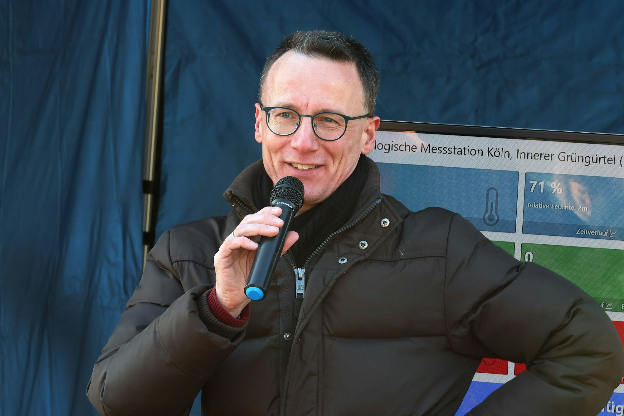 Der Professor in Winterjacke und mit runder Brille an einem Mikrofon.
