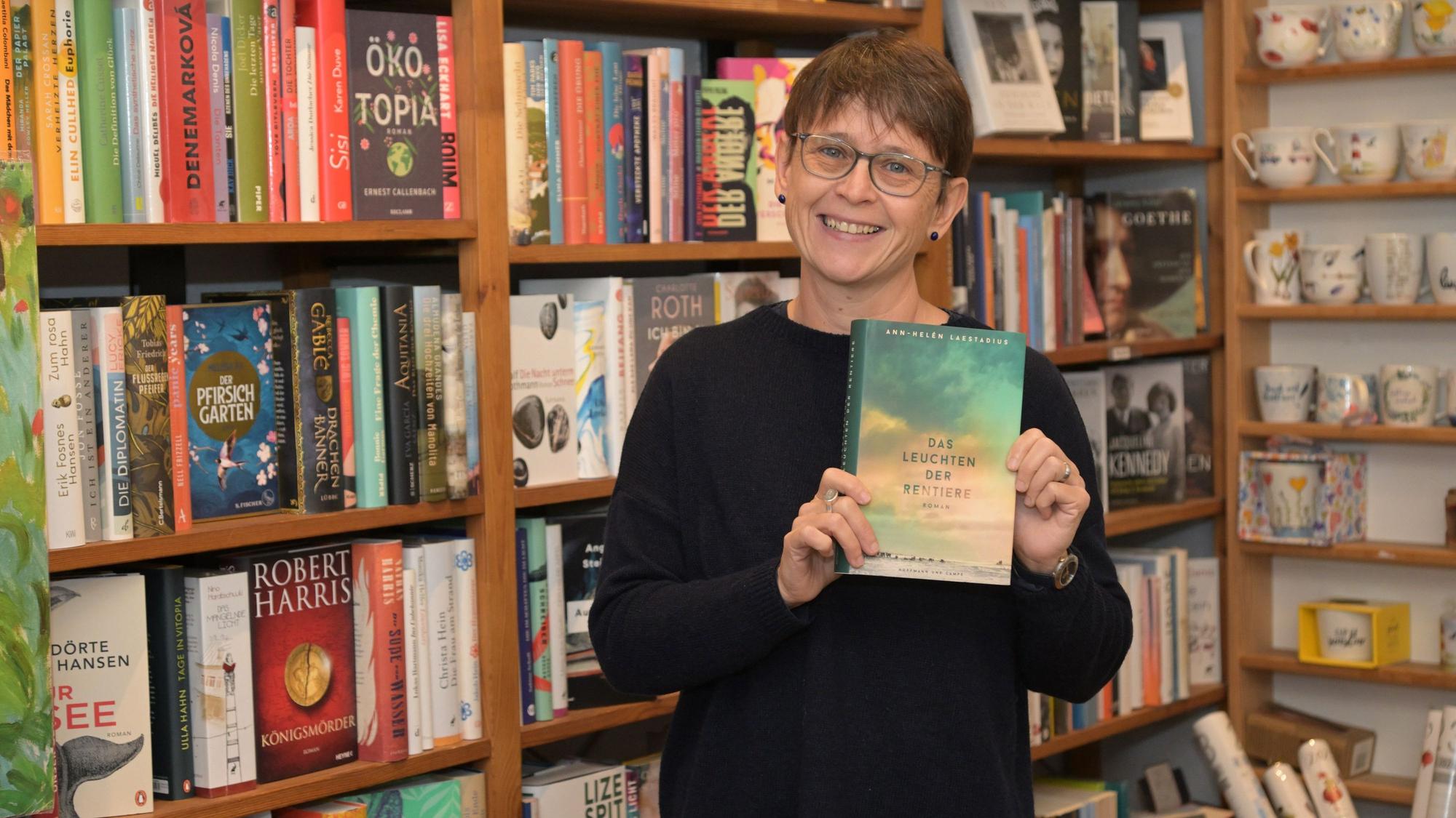 Michaele Rusch steht in der Ecke ihrer Buchhandlung und hält „Das Leuchten der Rentiere“ in der Hand.