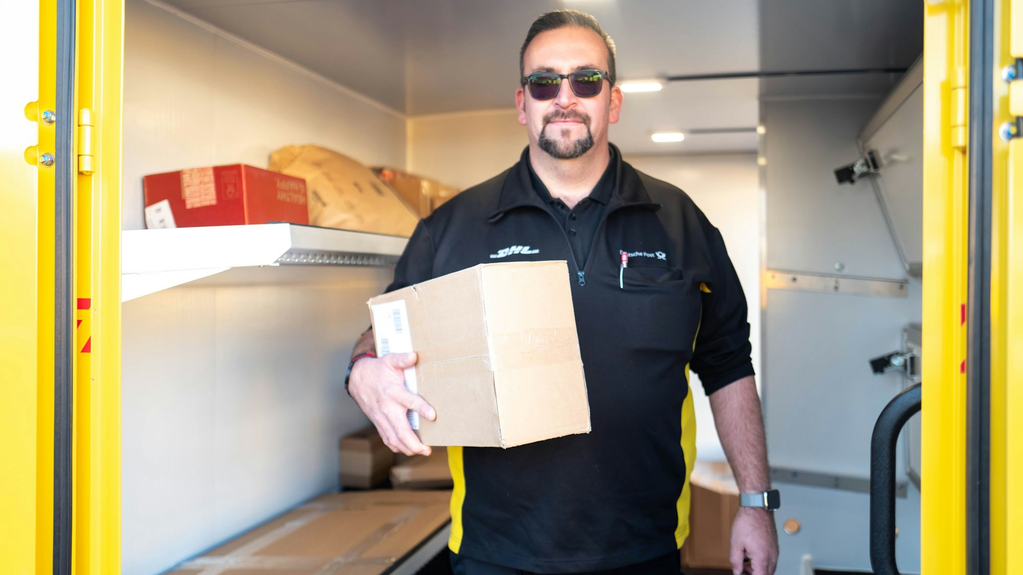 Zusteller Christoph Kompalke trägt ein Paket unter dem Arm und will gerade den neuen Streetscooter verlassen.