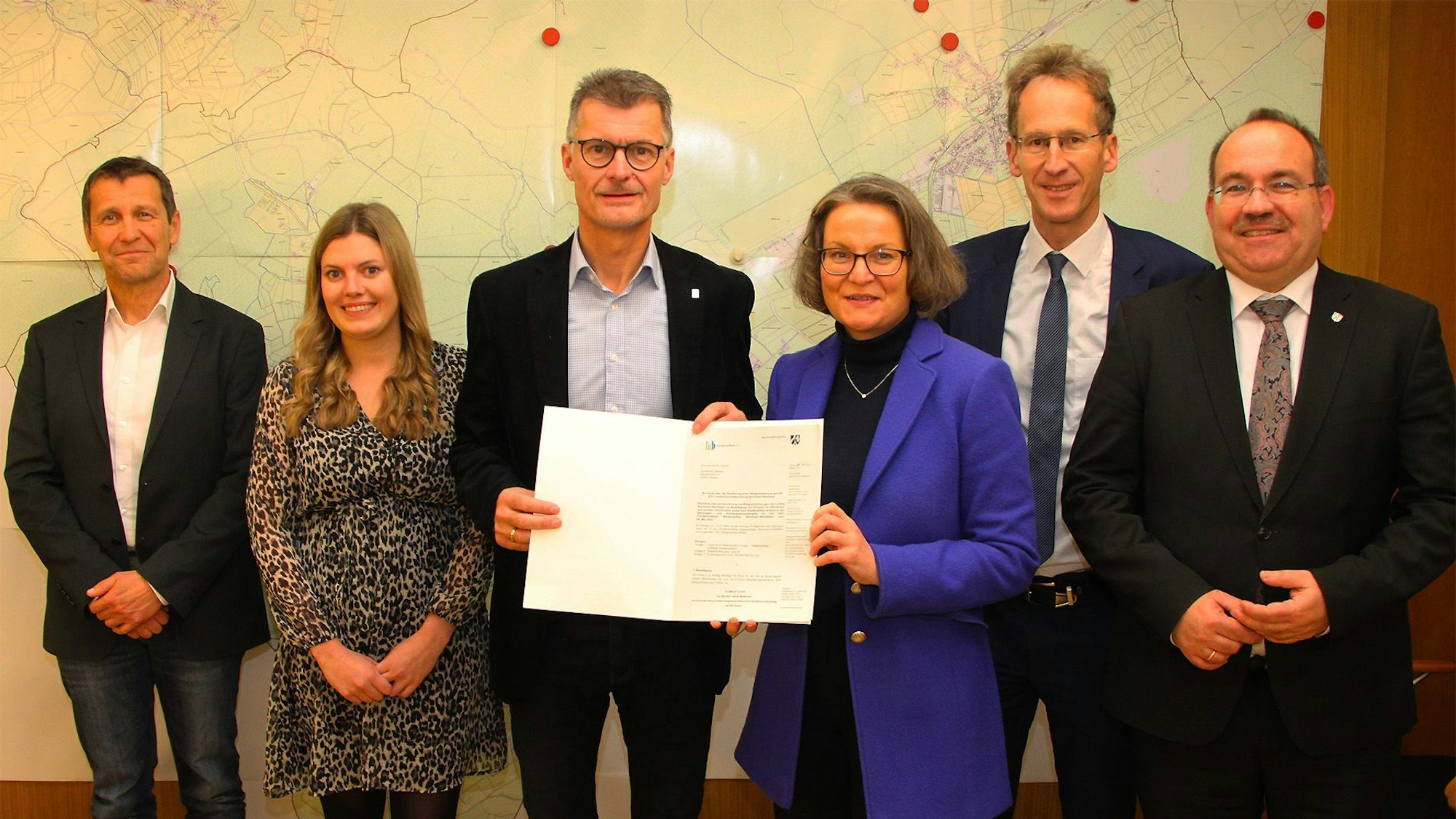 Ministerin Ina Scharrenbach überreicht Bürgermeister Jan Lembach im Schmidtheimer Rathaus den 13-Millionen-Euro Förderbescheid. Gemeinsam mit Erwin Bungartz, Melissa Brandt, Detlef Seif und Ralf Nolten posieren sie für ein Foto.