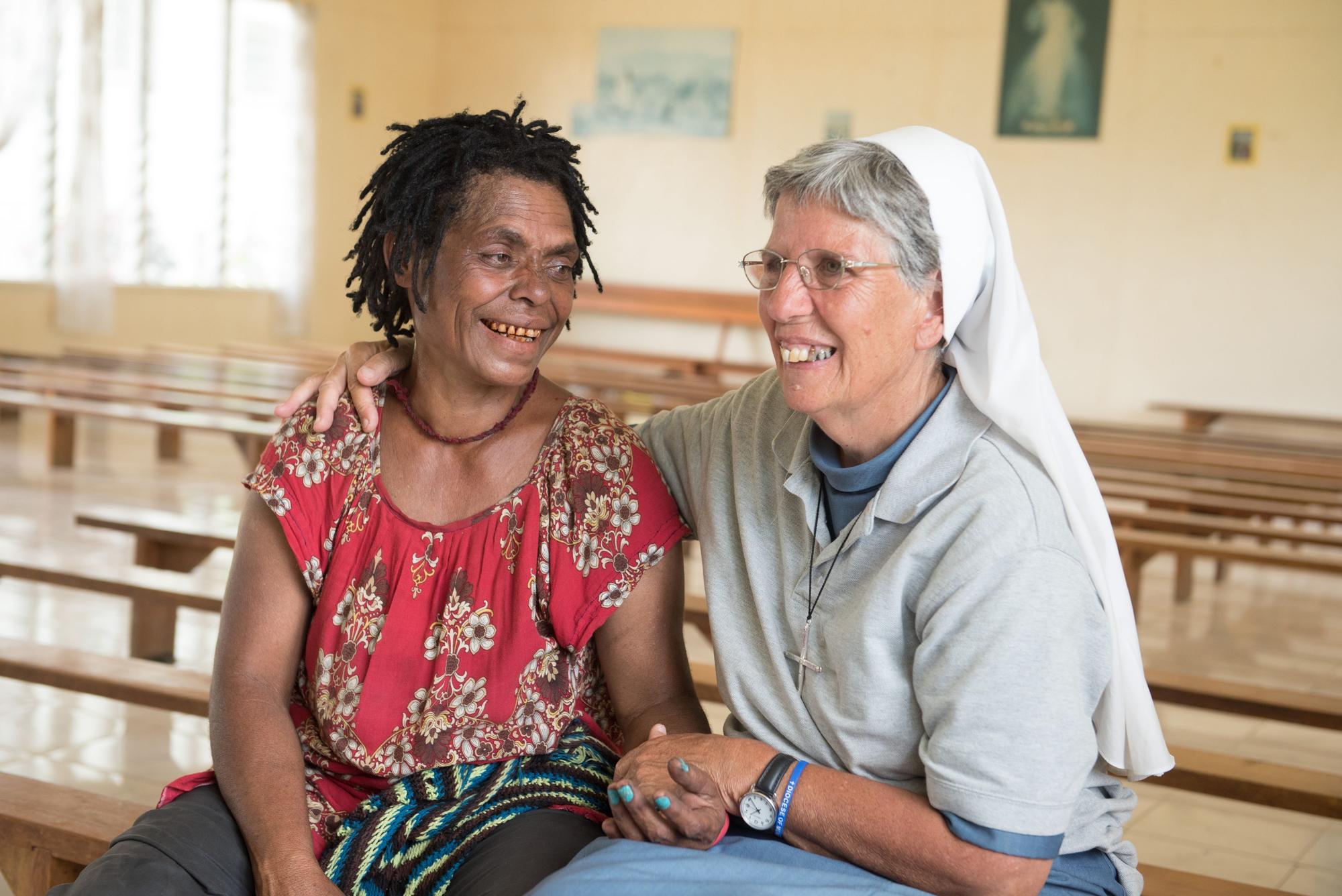 Die Ordensschwester Lorena Jenal sitzt mit der Überlebenden einer Hexenverbrennung in Papua Neuguinea in einer Kirche in Kundiawa und hält ihre Hand.