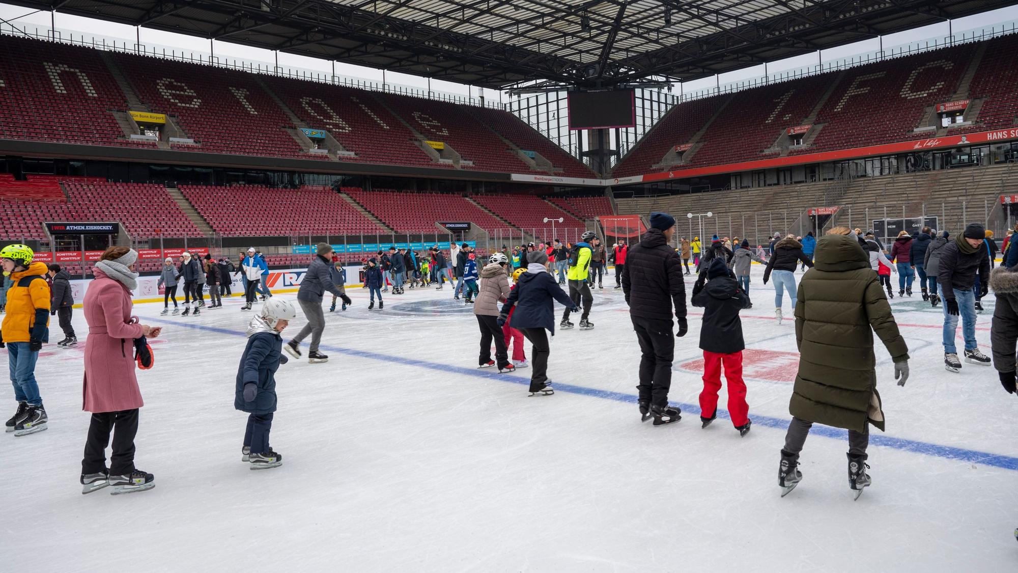 Menschen auf Schlittschuhen auf einer Eisfläche vor den leeren Rängen des Stadions