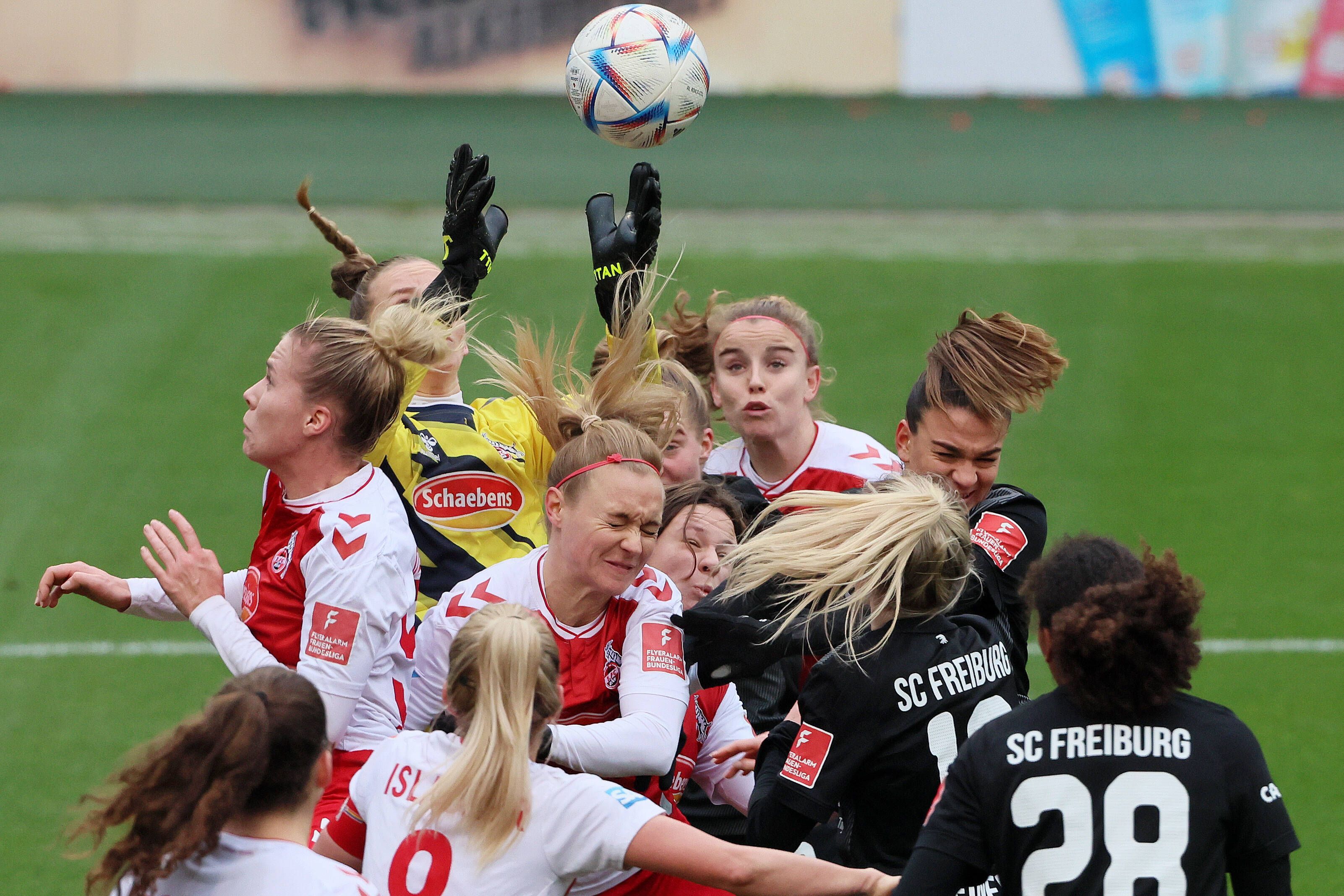 Eine Fußball-Torhüterin versucht, den Ball aus der Luft zu fangen, während sie von mehreren Spielerinnen umzingelt ist.