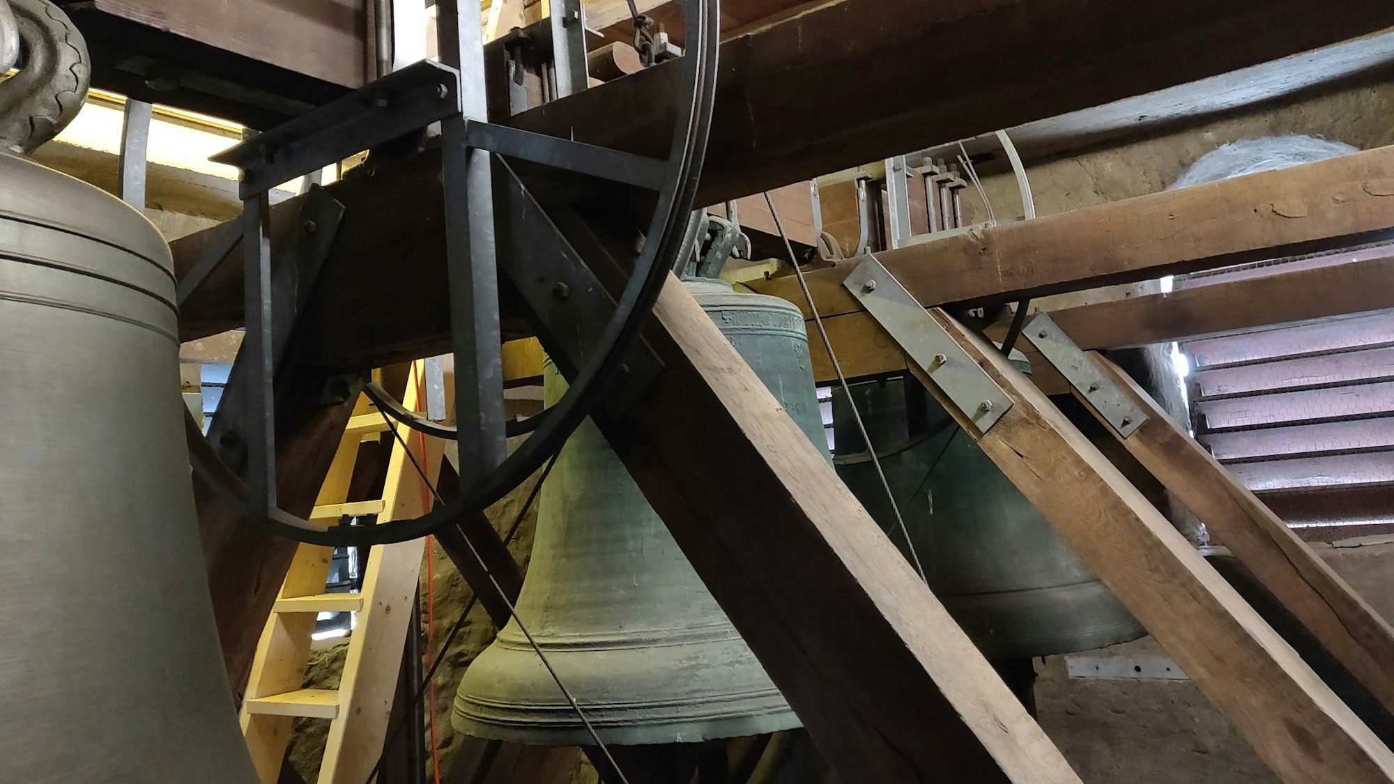 Im Dachstuhl der Kirche hängen drei Glocken nebeneinander an Holzbalken.