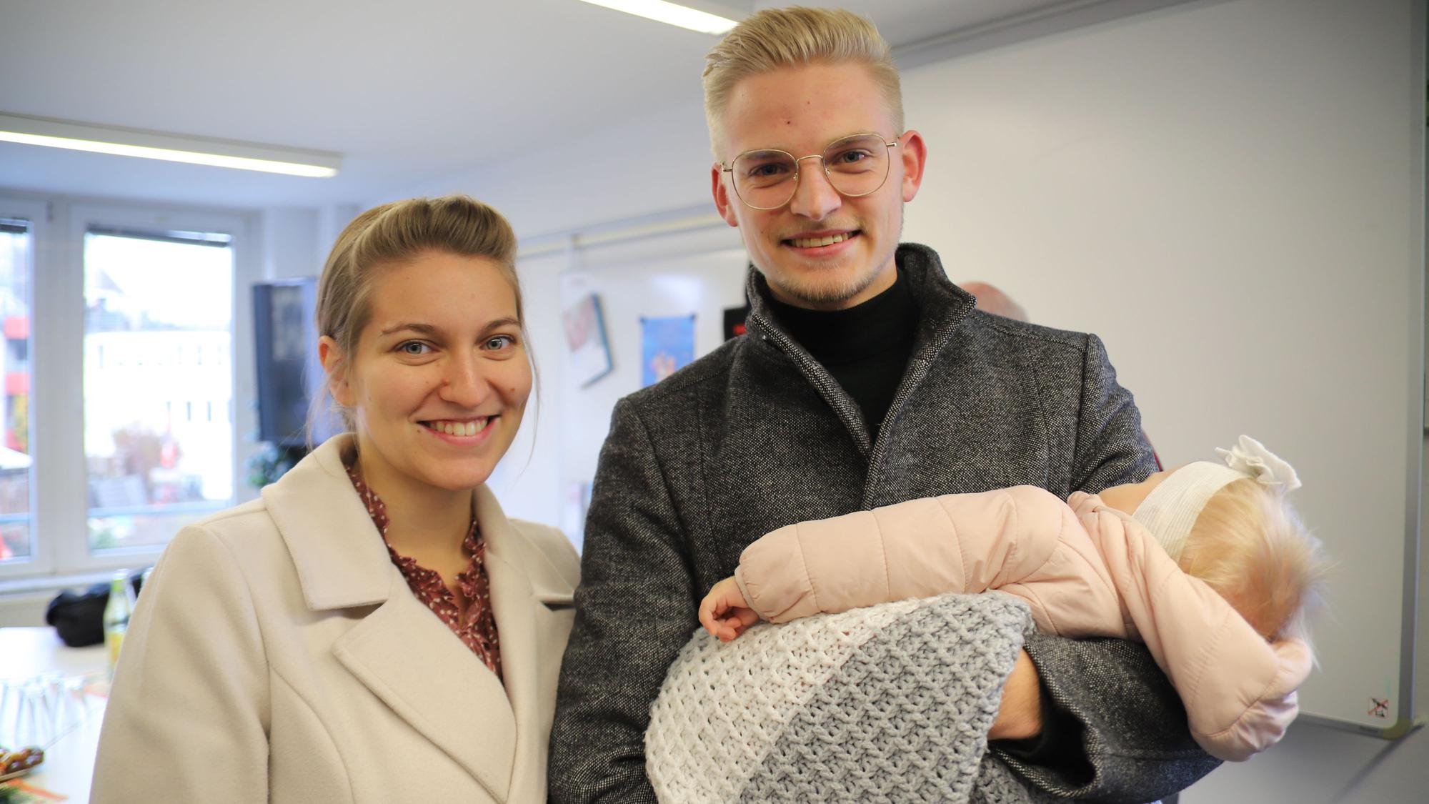Eine Frau und ein Mann lachen in die Kamera. Der Mann hat ein Baby auf dem Arm.