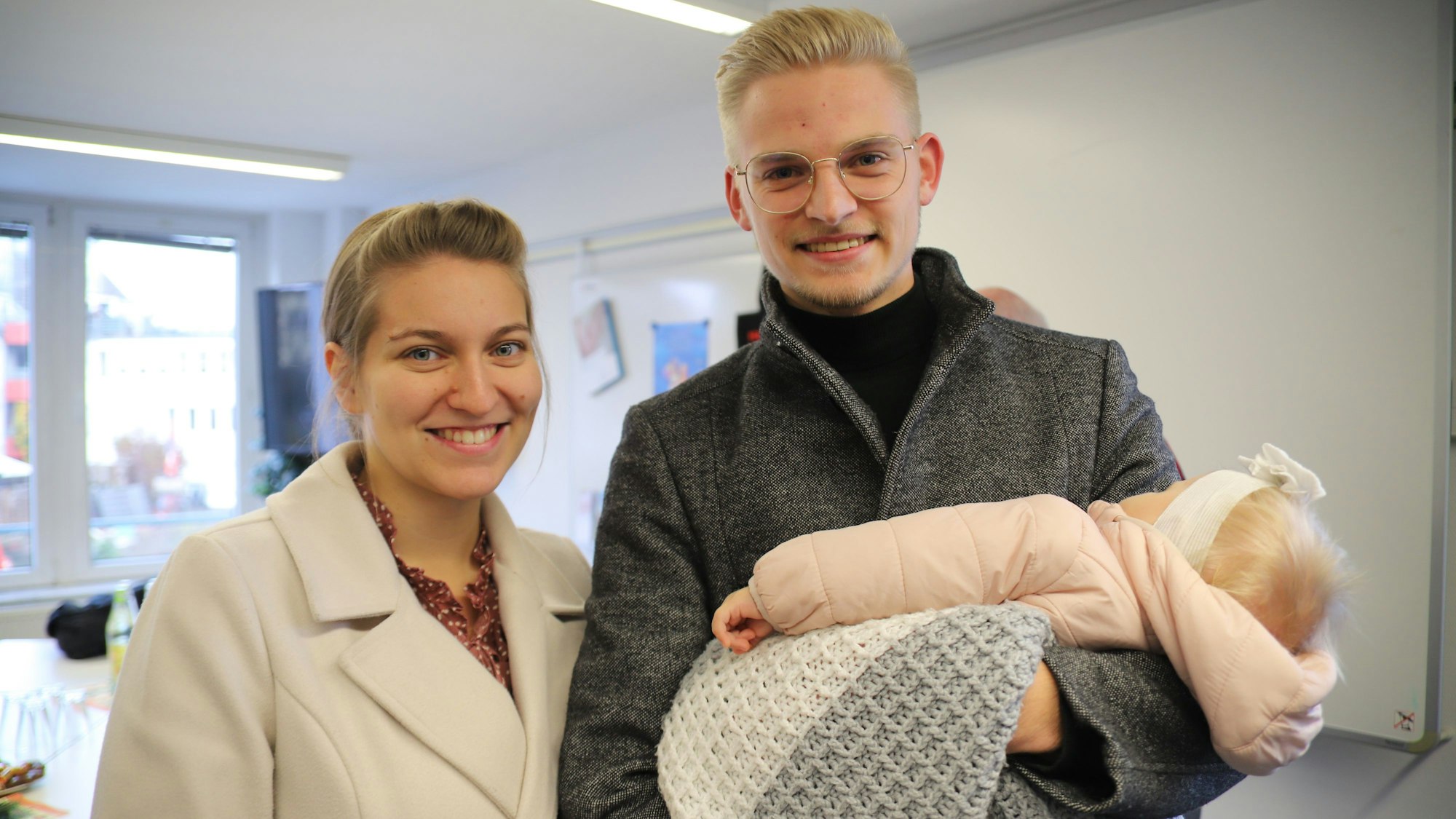 Eine Frau und ein Mann lachen in die Kamera. Der Mann hat ein Baby auf dem Arm.