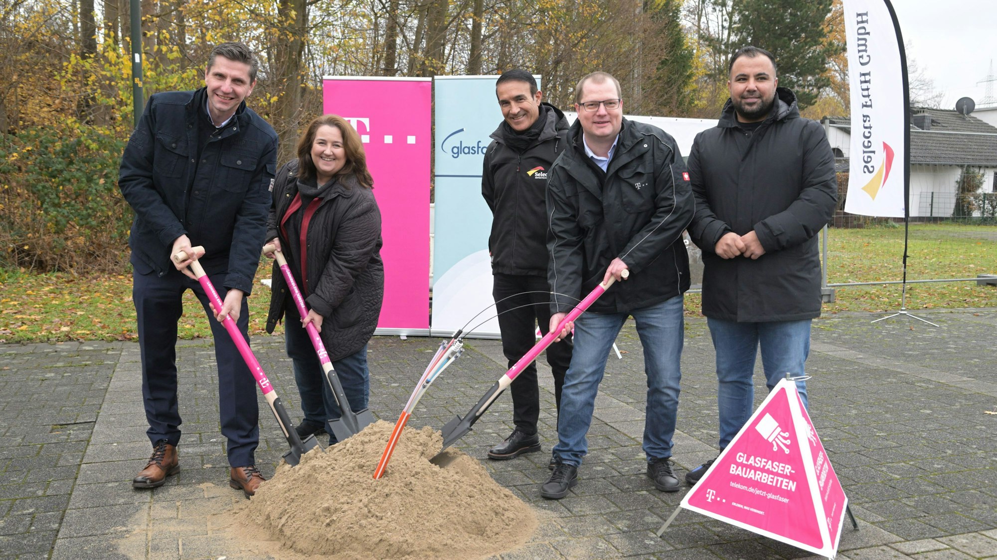 Vier Männer und Bondina Schulze, Bürgermeisterin von Rösrath, stoßen symbolisch einen Spaten in ein Sandhäufchen, aus dem Glasfasern ragen.