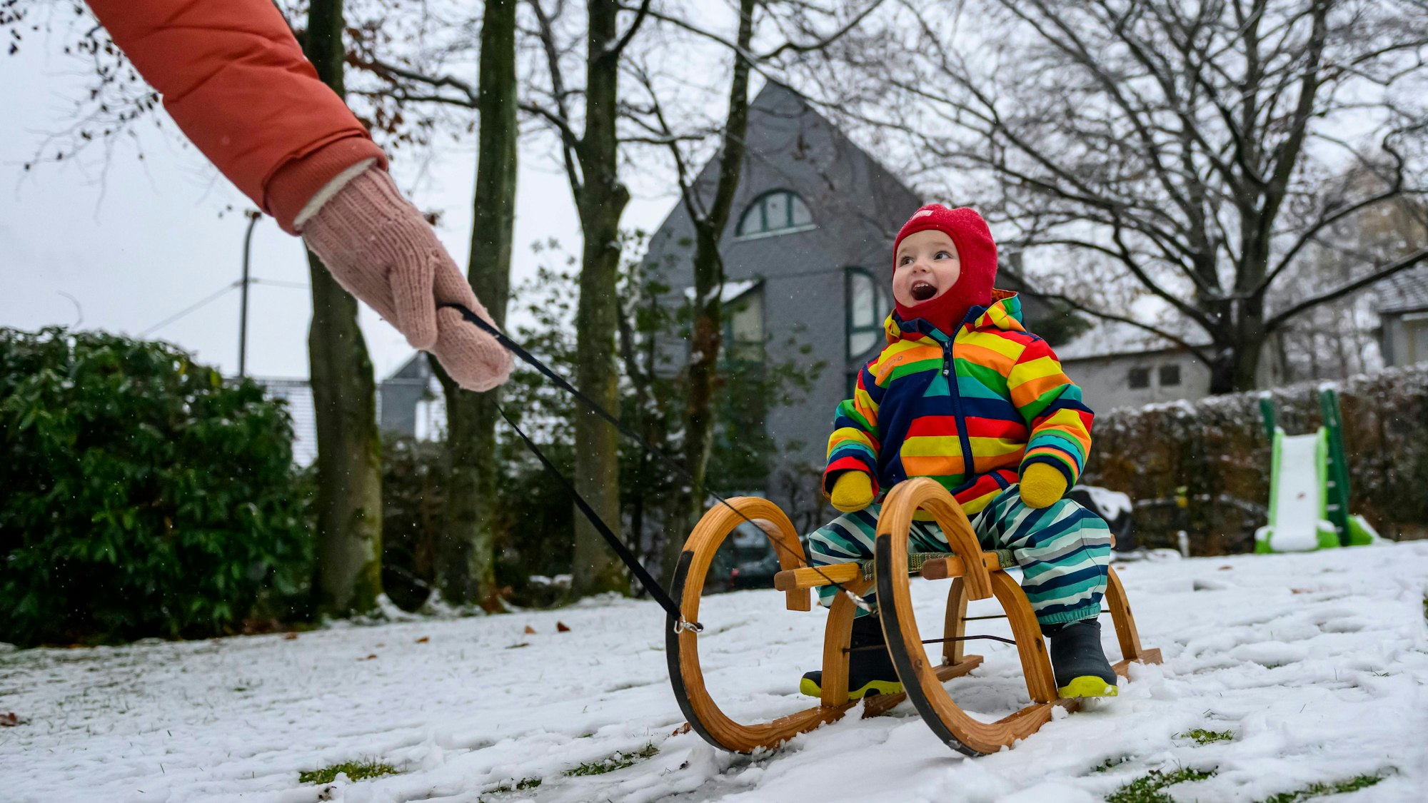 Ein Kind fährt mit der Mutter im heimischen Garten Schlitten im Schnee, nach Wintereinbruch und erstem Schneefall in Remscheid Lennep.