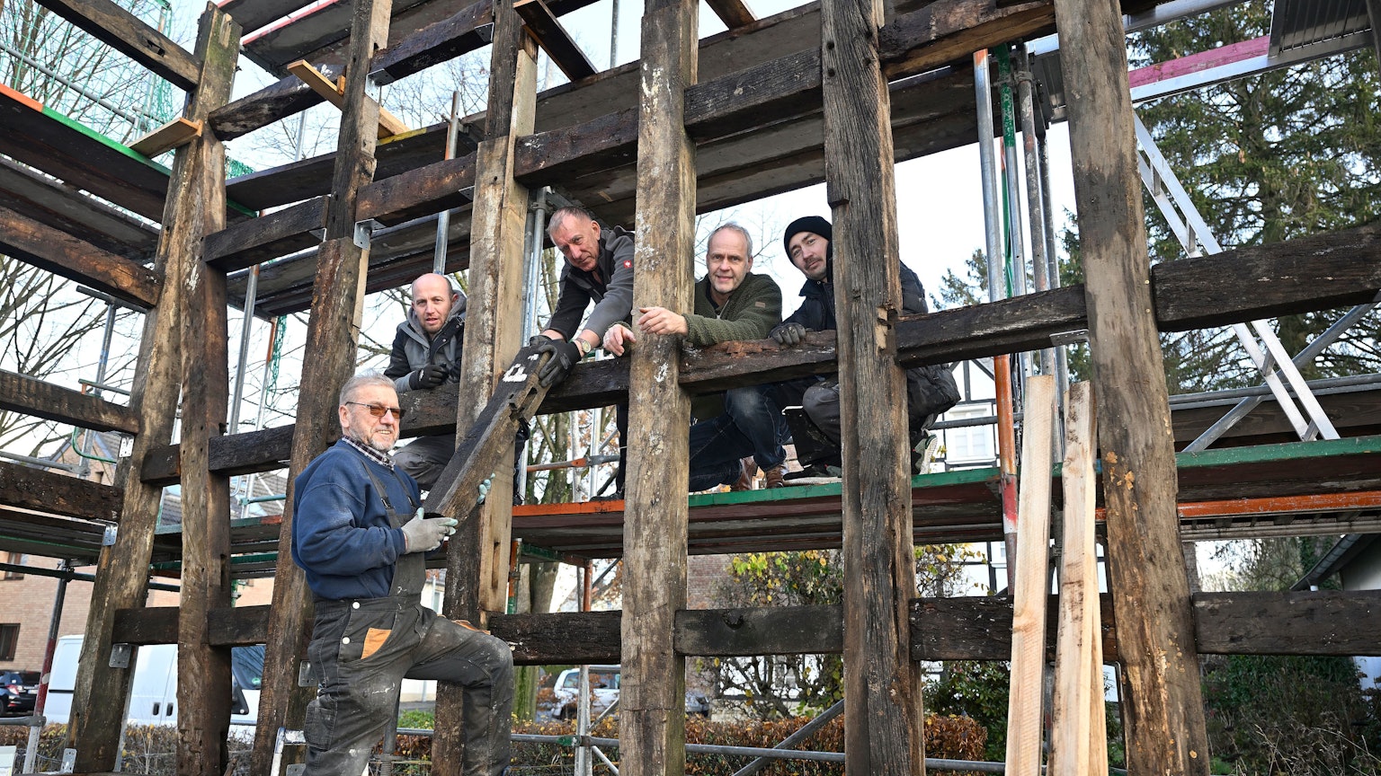 Markus Hetzenegger steht mit vier weiteren Handwerkern zwischen den Holzbalken eines noch unfertigen Fachwerkhauses.