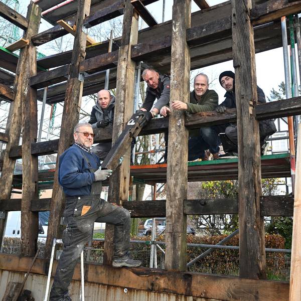 Markus Hetzenegger steht mit vier weiteren Handwerkern zwischen den Holzbalken eines noch unfertigen Fachwerkhauses.