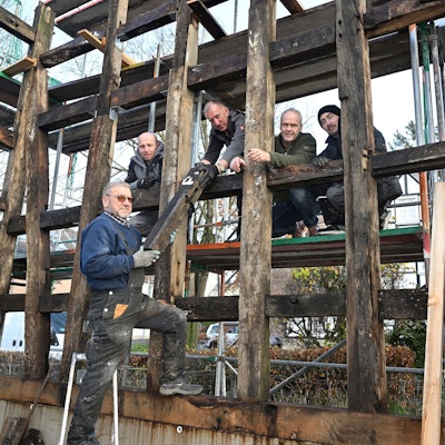 Markus Hetzenegger steht mit vier weiteren Handwerkern zwischen den Holzbalken eines noch unfertigen Fachwerkhauses.