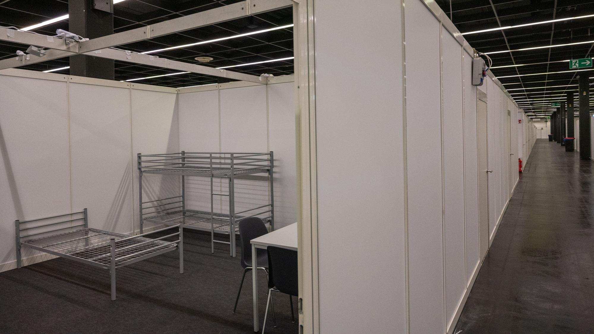 Eine Unterkunft für Geflüchtete in der Koelnmesse. Ein Bett und ein Hochbett sowie ein Tisch mit Stühlen steht auf der Fläche.