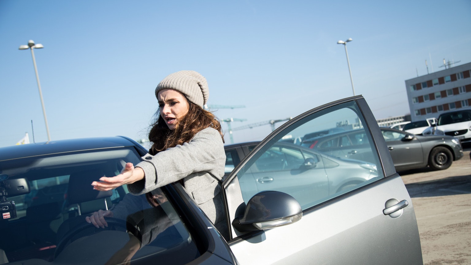 Eine Frau mit Mütze steht an ihrer Autotür und streckt wütend den Arm aus.