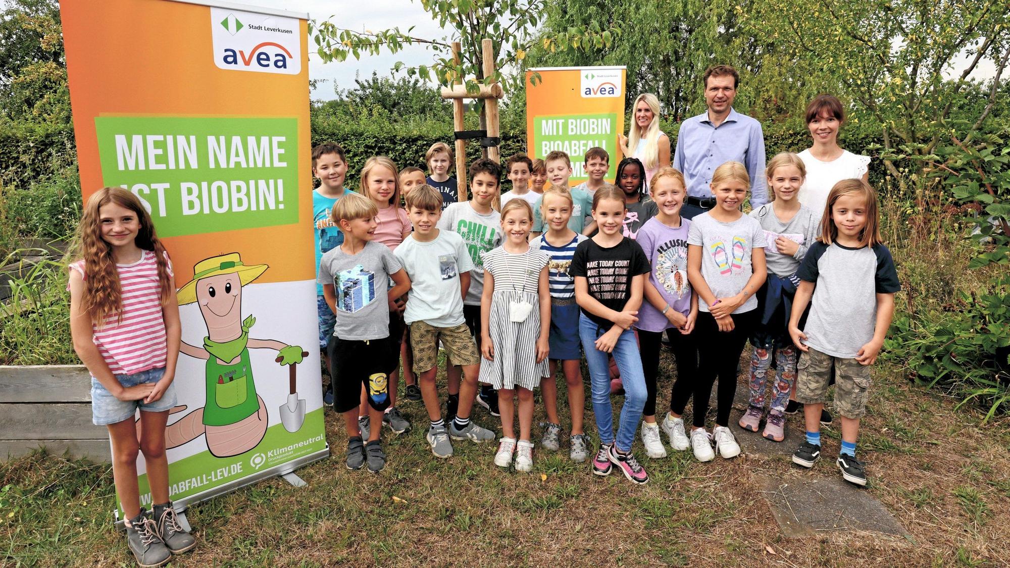 Kinder haben sich im Hitdorfer Kleingarten vor Plakaten mit dem Biotonnen-Maskottchen Biobin aufgestellt.