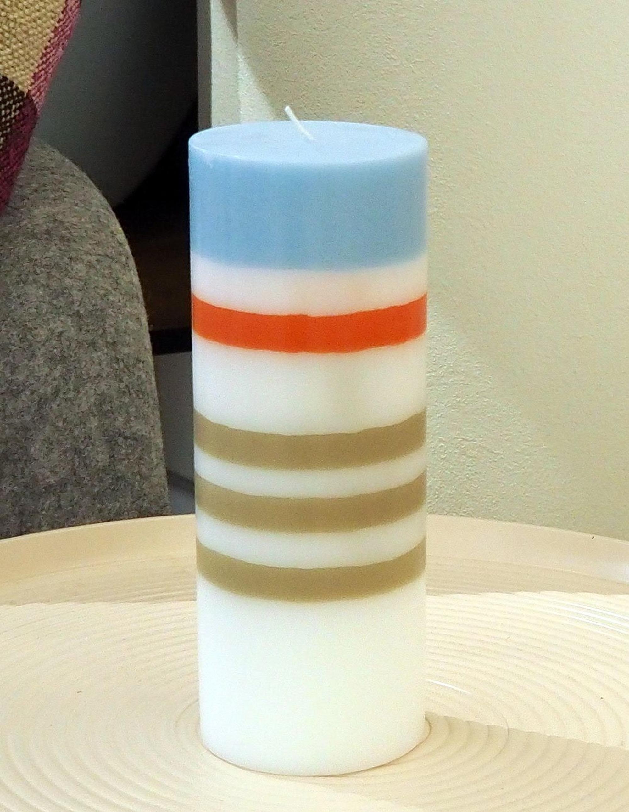 Eine weiße Kerze mit braunen, roten und blauen Streifen.