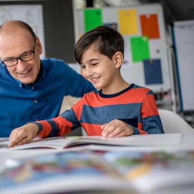 Mentor Andreas Endermann begleitet ein Kind beim Lesenlernen - das Bild zeigt die beiden, wie sie in einem Buch lesen, das vor ihnen auf dem Tisch liegt.