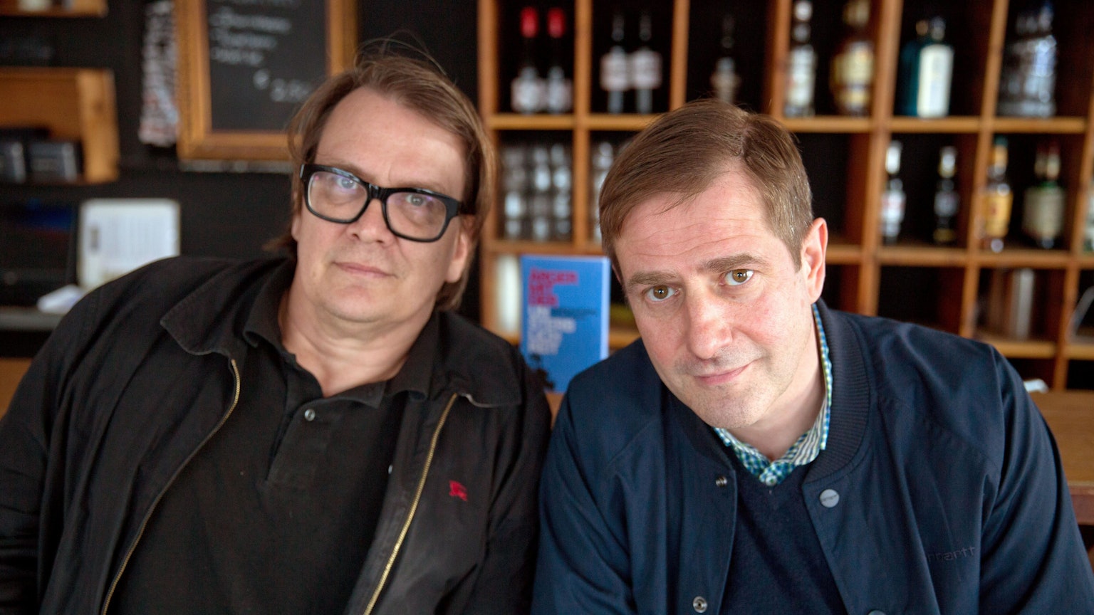 Die Autoren Sven Regener (links) und Andreas Dorau sitzen vor einem Bücherregal.