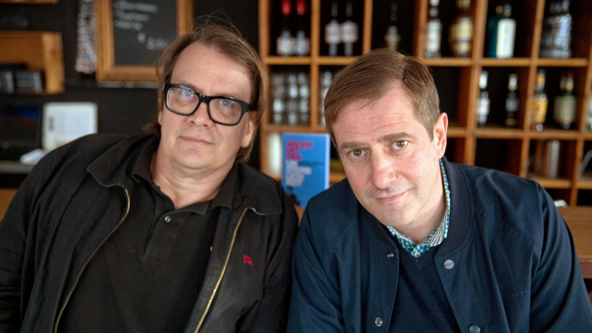 Die Autoren Sven Regener (links) und Andreas Dorau sitzen vor einem Bücherregal.
