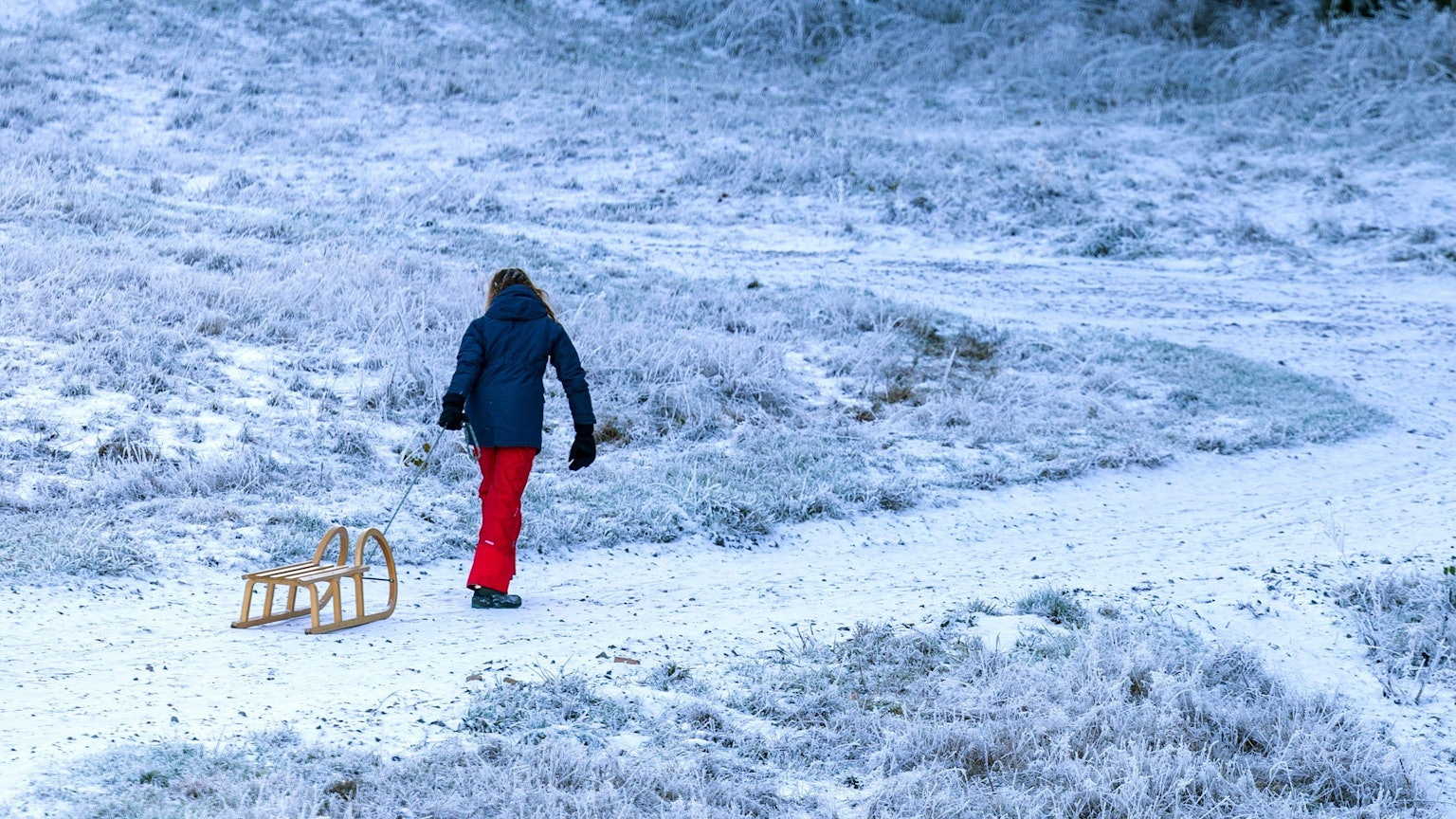 Eine junge Frau zieht einen Schlitten einen Berg hinauf.