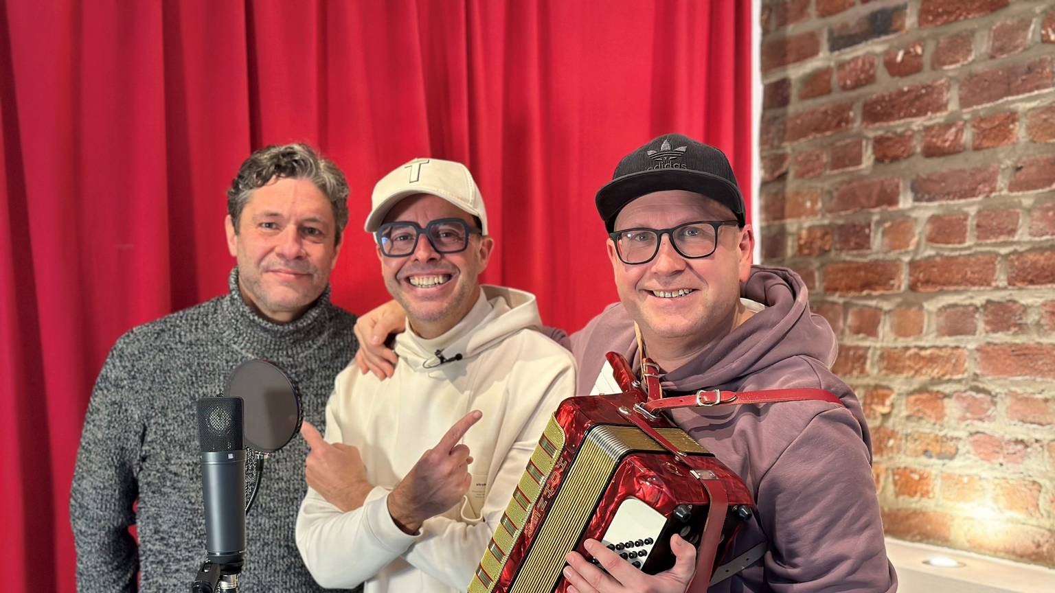 Anno Thenenbach, Till Quitmann und Christian Kock posieren vor einem Mikrofon.