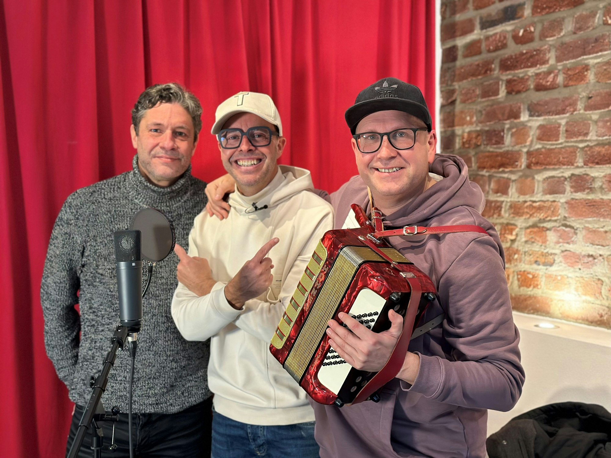 Anno Thenenbach, Till Quitmann und Christian Kock posieren vor einem Mikrofon.