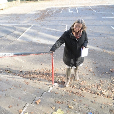Die Schulleiterin steht vor der Schule am Treppengeländer.