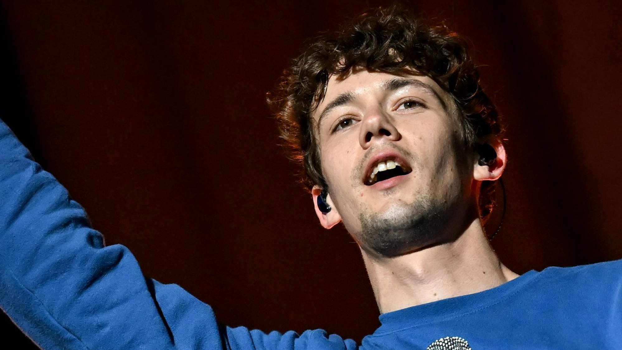 Der Sänger und Frontmann der Band AnnenMayKantereit, Henning May, steht auf der Bühne und hält ein Mikrofon in der Hand, die andere streckt er in die Luft.