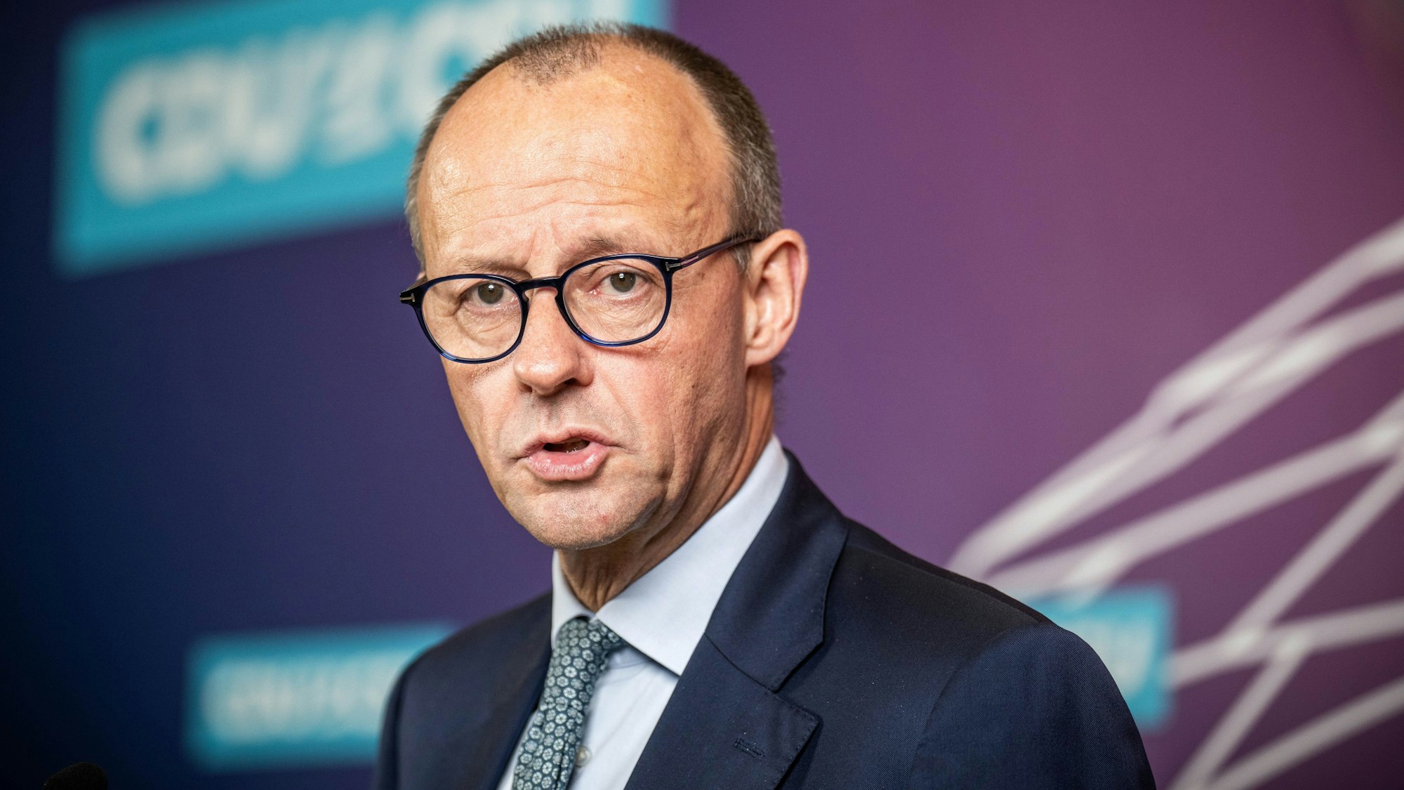 Friedrich Merz steht in dunkelblauem Anzug vor einer Wand, er blickt besorgt.