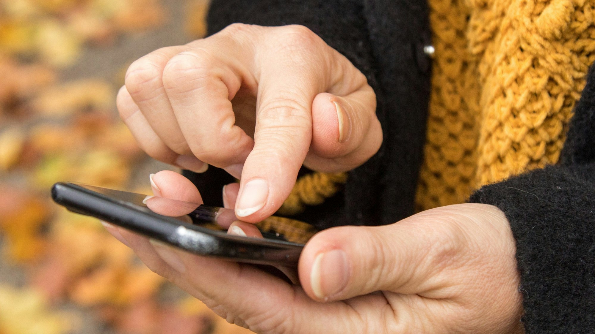 Eine Person hält ein Smartphone in der Hand und tippt darauf.