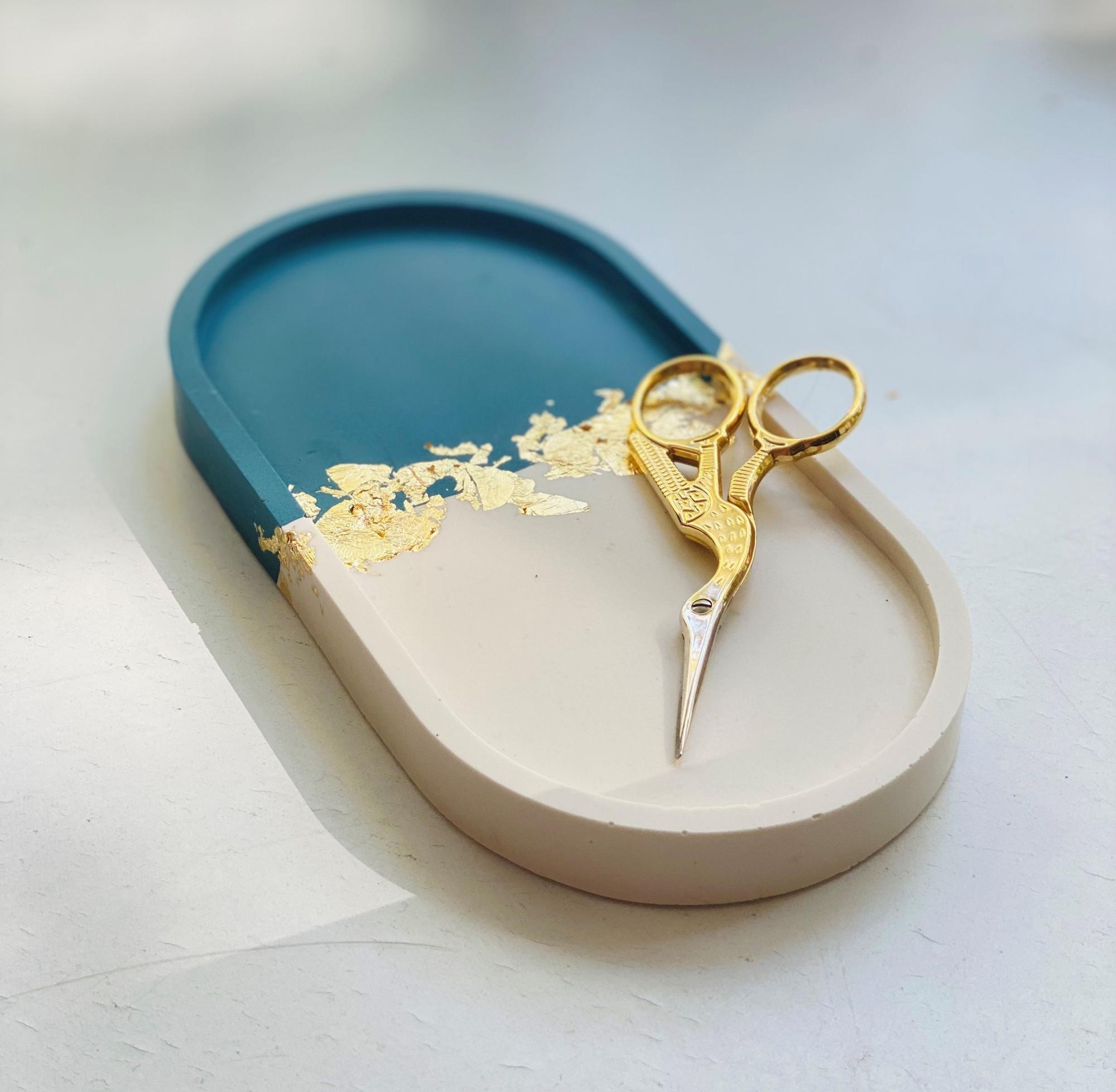 Blau-weiß-goldene Schale von „The Werkstatt“ mit goldener Schere darauf.