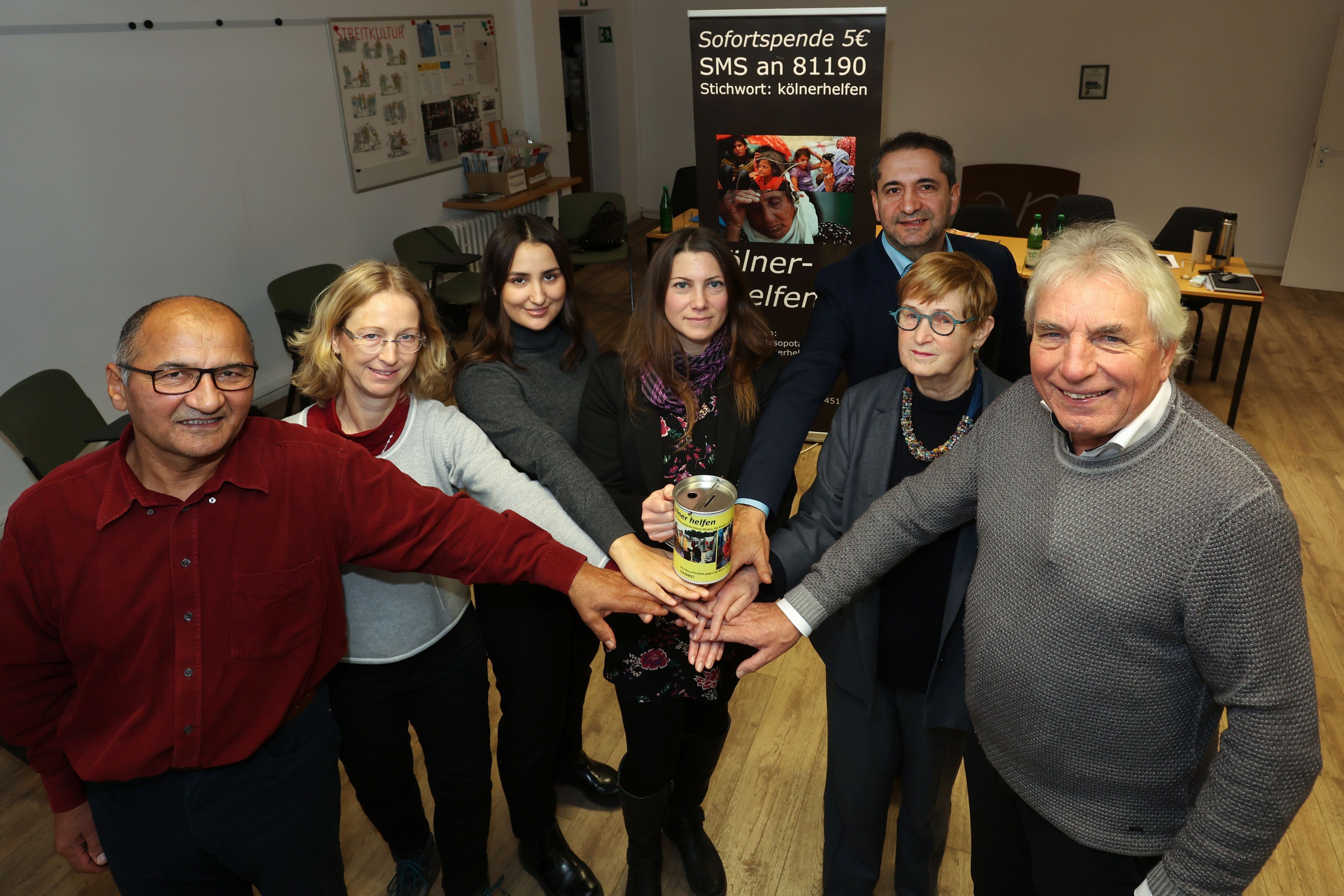 Ali Gececi, Dorothee Zimmer-Gececi, Anna Gececi, Berit Kranz, Vedat Akfer, Anke Brunn und Jürgen Roters der Initiative „Kölner helfen" halten gemeinsam eine Spenden-Spardose.