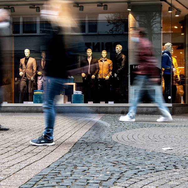 Verschwommene Personen gehen an einem Anziehsachen-Geschäft vorbei