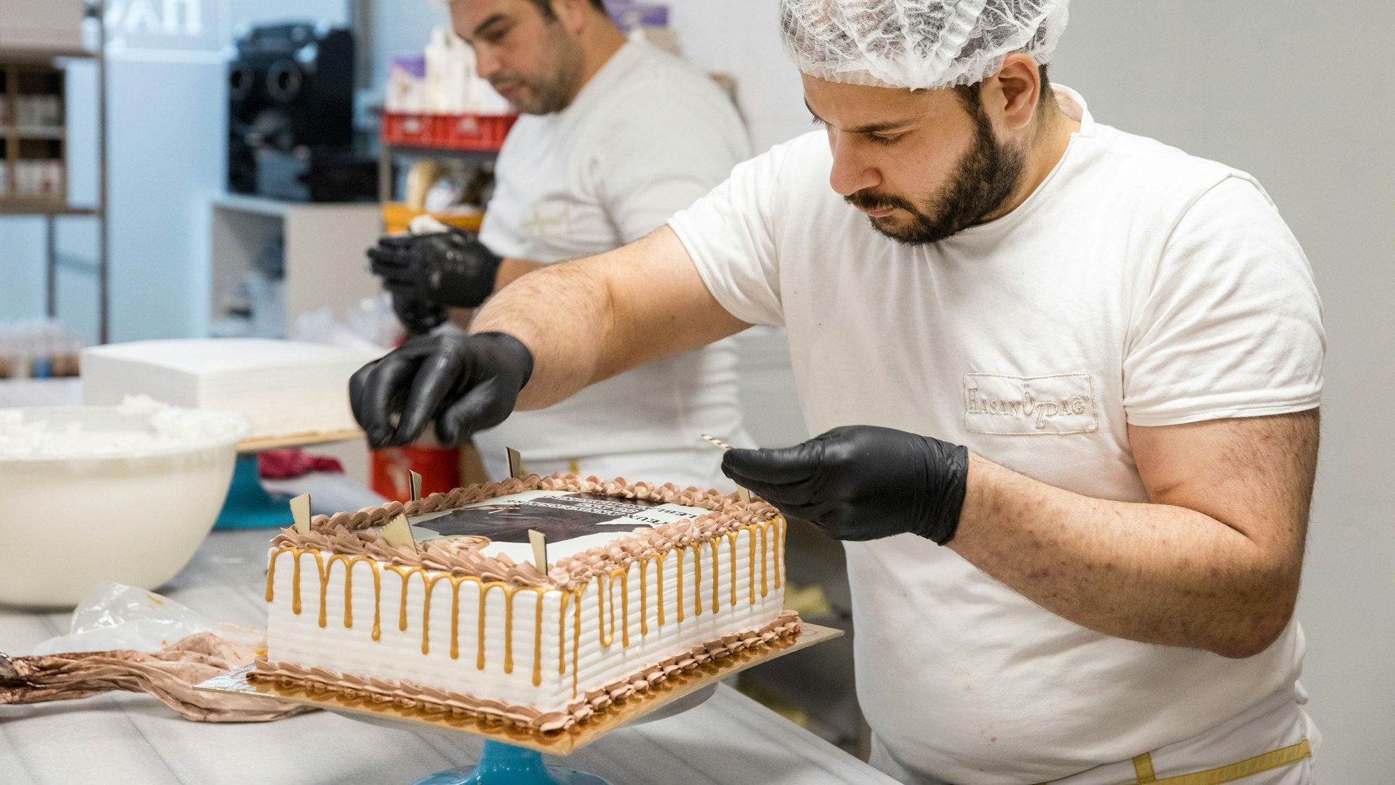Ein Mitarbeiter dekoriert eine Torte mit Drip-Effekt, bei dem der Guss an den Rändern herunterläuft.