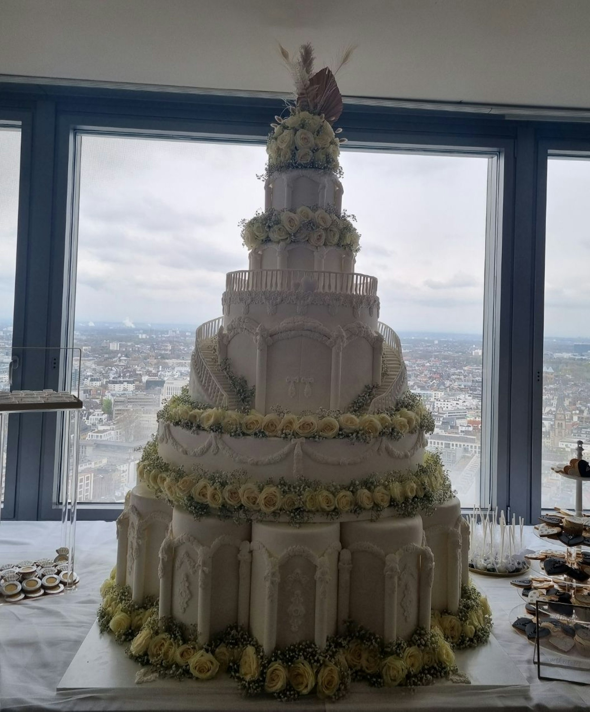 Eine 1,50 Meter hohe, mit Blumen verzierte Hochzeitstorte ist vor dem Kölner Panorama zu sehen.