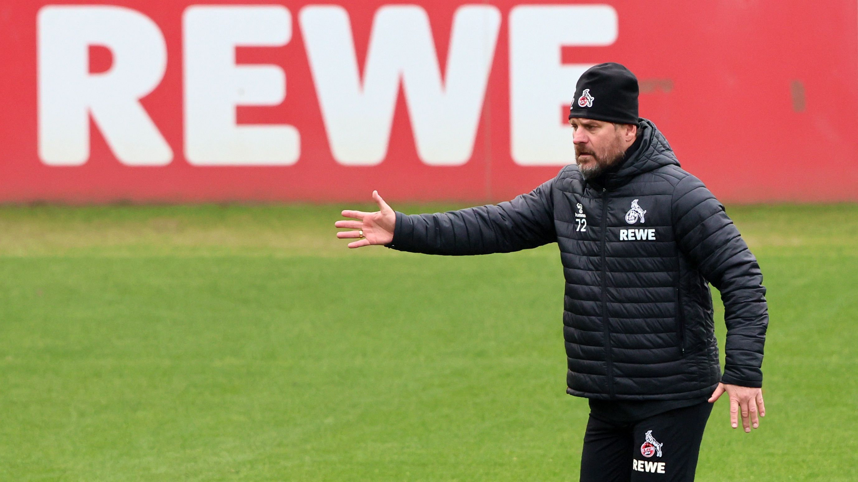 Steffen Baumgart steht mit Mütze auf dem Trainingsplatz des 1. FC Köln und gibt seinen Spielern Anweisungne.
