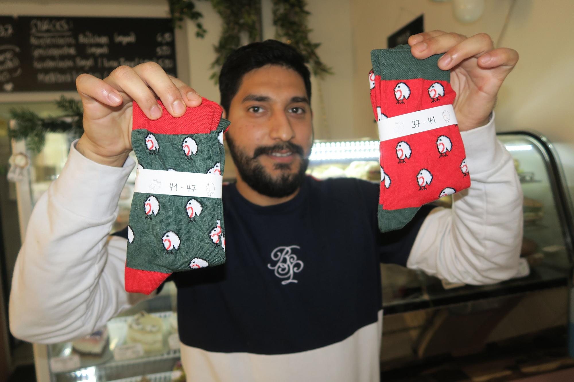 Ein Mitarbeiter im Café Rotkehlchen hält zwei Paar der Socken in die Kamera.