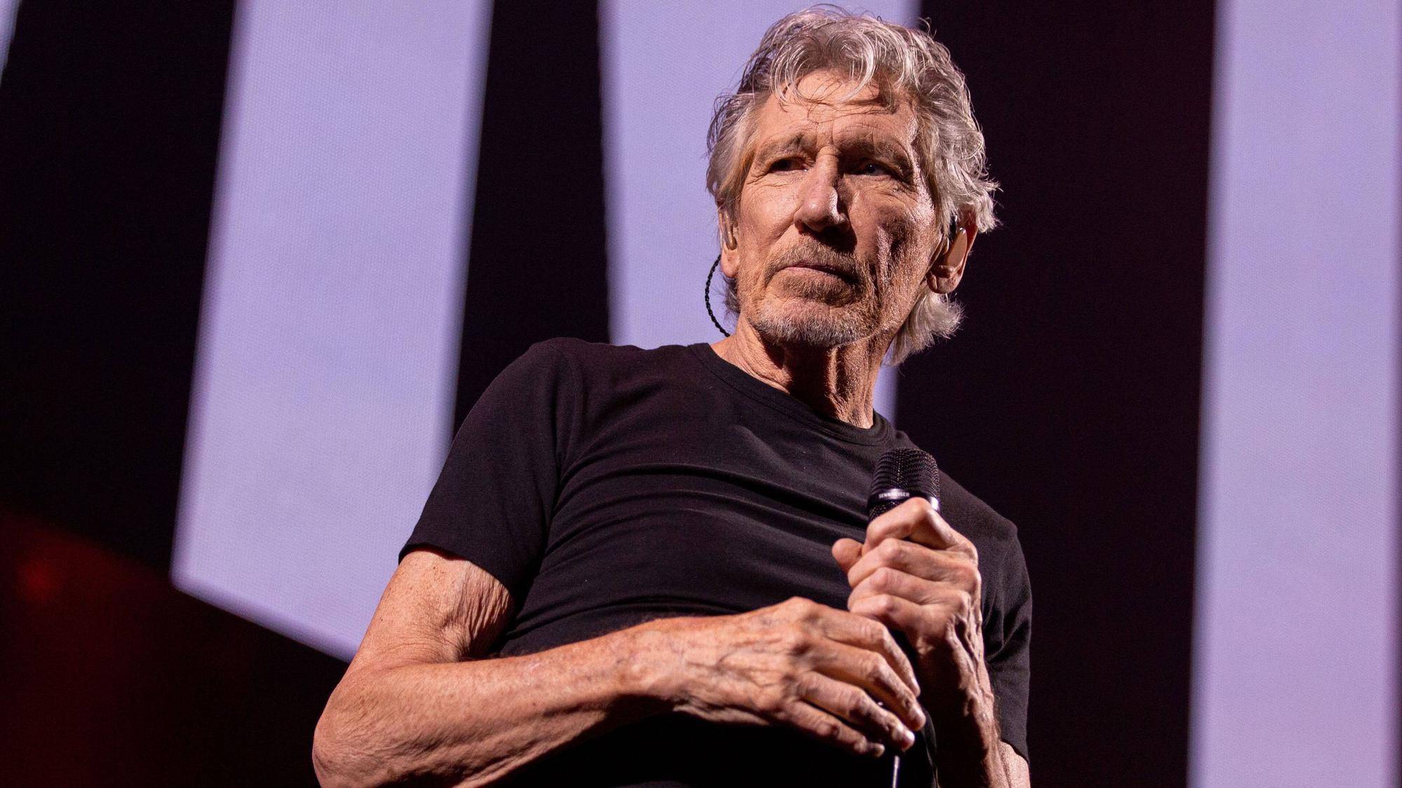 Roger Waters steht im schwarzen T-Shirt auf einer Konzertbühne.